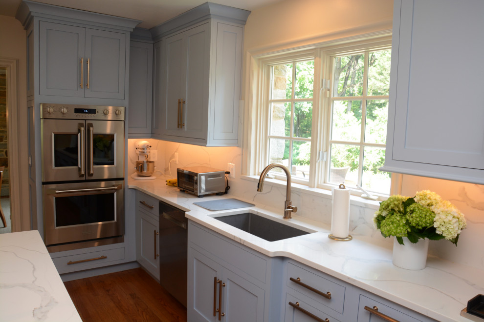 Inspiration for a mid-sized transitional u-shaped separate kitchen in Baltimore with an undermount sink, shaker cabinets, blue cabinets, quartz benchtops, white splashback, engineered quartz splashback, stainless steel appliances, medium hardwood floors, with island, brown floor and white benchtop.