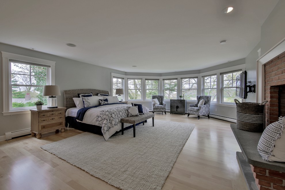 This is an example of an expansive transitional master bedroom in Boston with green walls, light hardwood floors, a standard fireplace, a brick fireplace surround and beige floor.