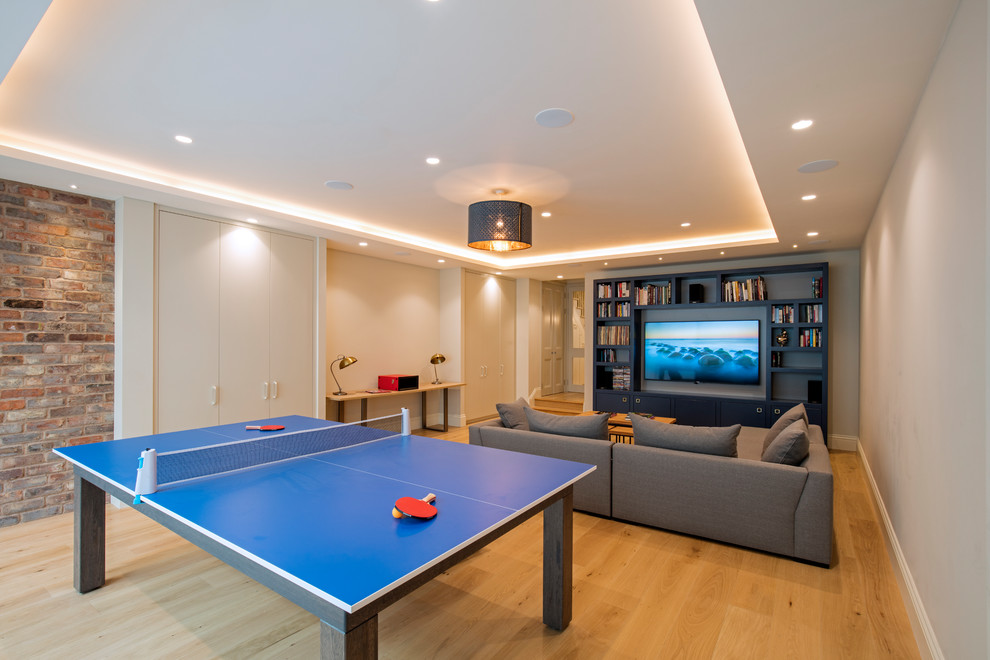 This is an example of a large contemporary open concept family room in London with a game room, white walls, light hardwood floors, a wall-mounted tv and beige floor.