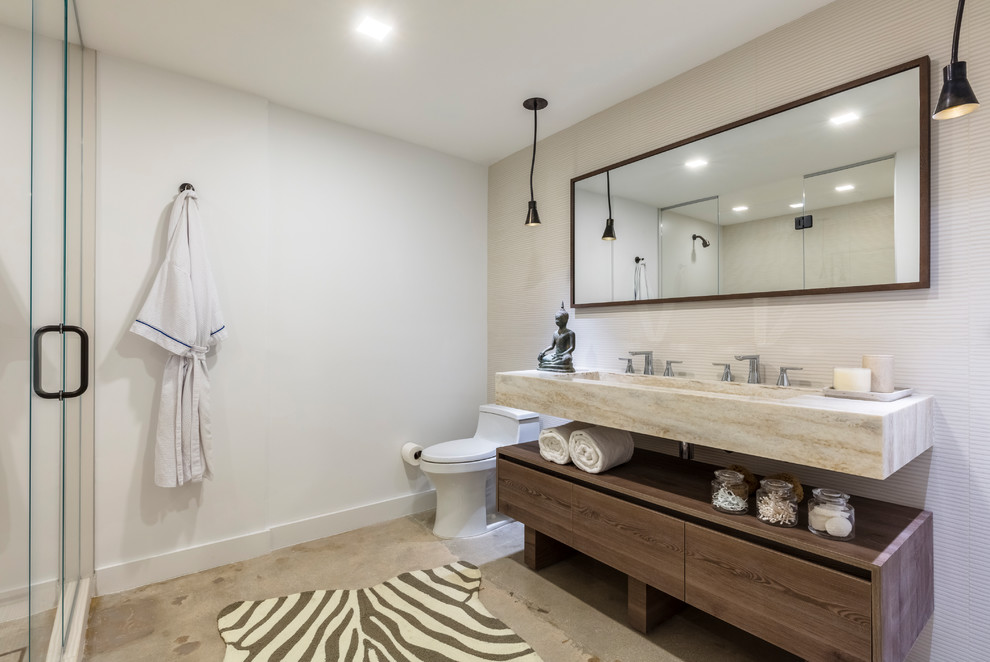 Photo of a mid-sized modern master bathroom in Miami with flat-panel cabinets, dark wood cabinets, an alcove shower, a one-piece toilet, beige tile, white walls, concrete floors, a trough sink, onyx benchtops, grey floor, a hinged shower door and beige benchtops.