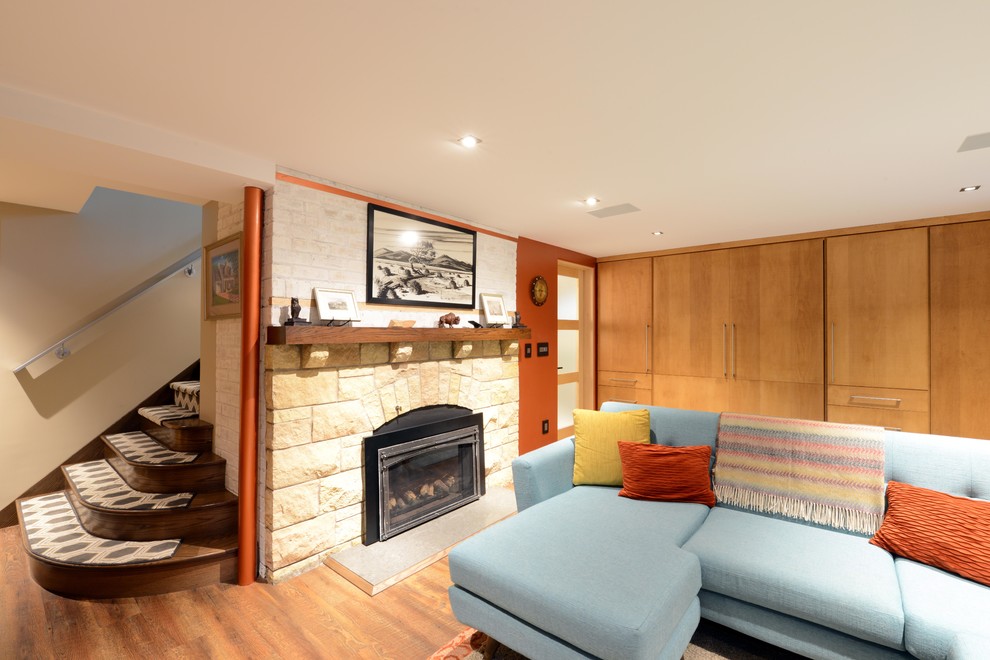 Design ideas for a small midcentury look-out basement in Other with beige walls, medium hardwood floors, a standard fireplace, a stone fireplace surround and beige floor.