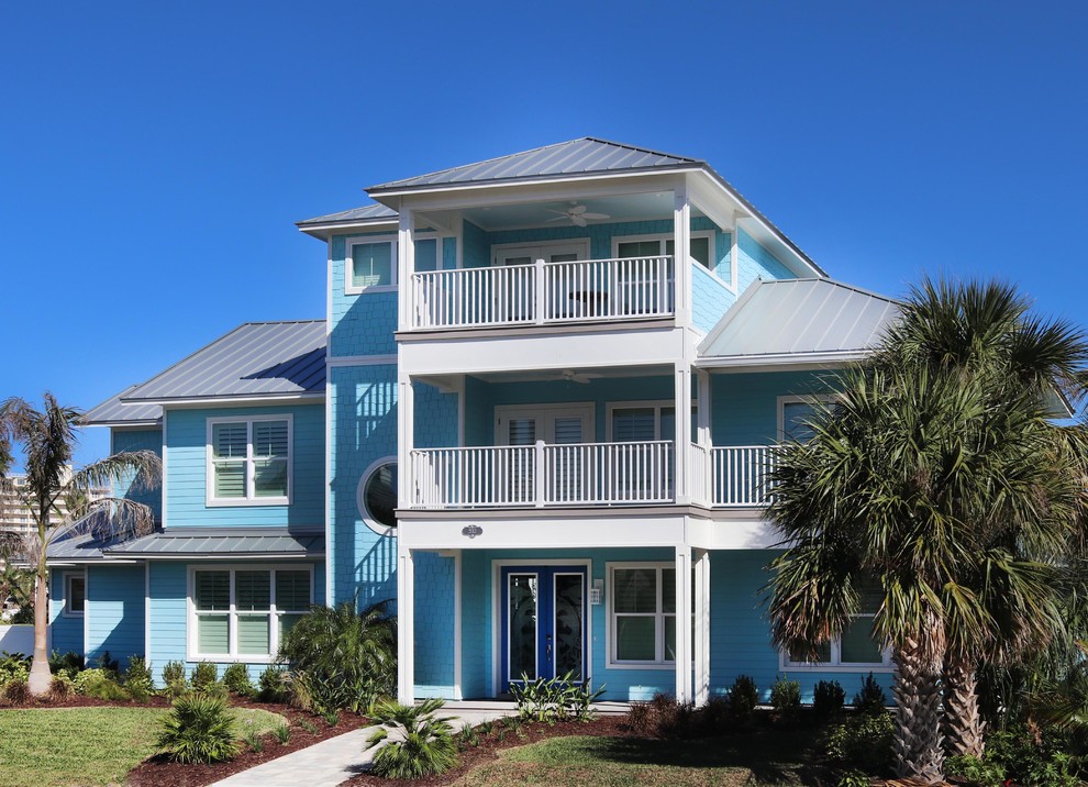 This is an example of a large beach style three-storey blue house exterior in Orlando with wood siding, a hip roof and a metal roof.