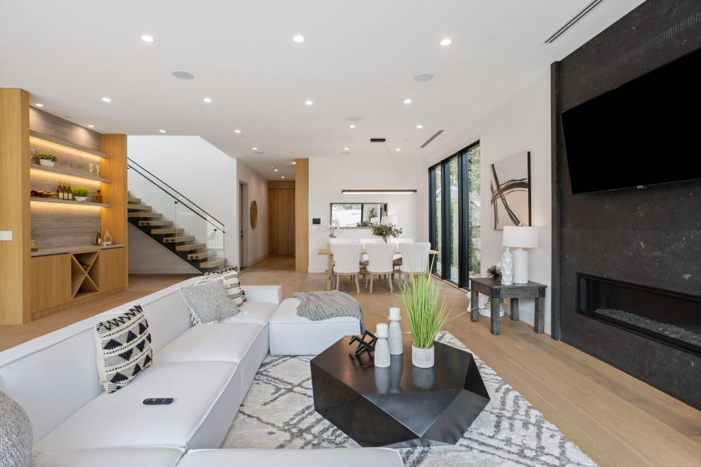Offenes Modernes Wohnzimmer mit hellem Holzboden, Kaminumrandung aus Stein und TV-Wand in Los Angeles