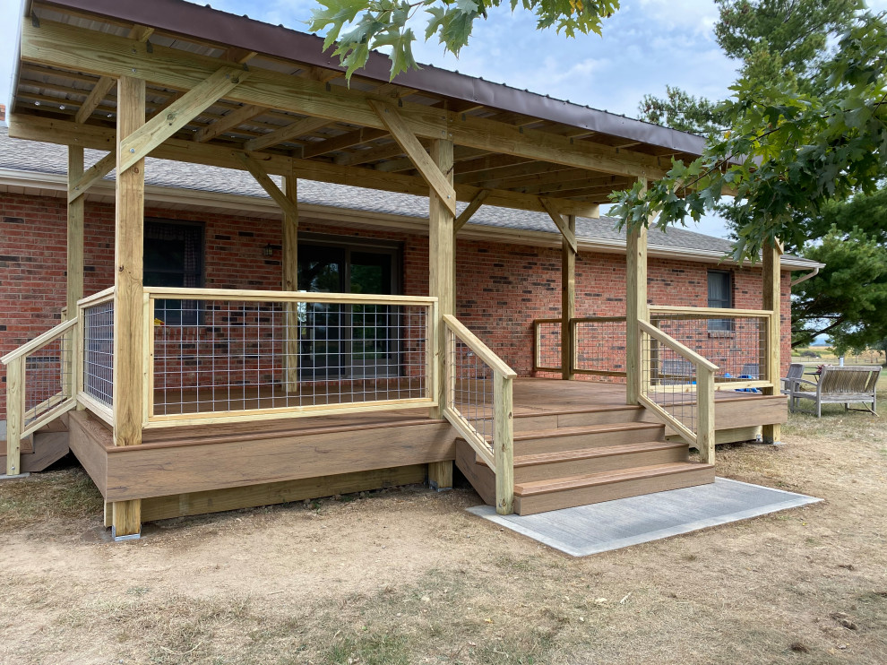 Modelo de terraza planta baja de estilo de casa de campo grande en patio trasero con pérgola y barandilla de varios materiales
