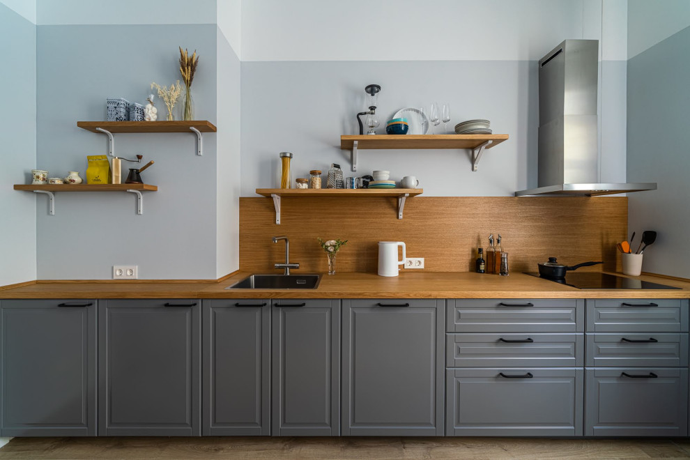 Design ideas for a mid-sized scandinavian single-wall eat-in kitchen in Saint Petersburg with a drop-in sink, raised-panel cabinets, grey cabinets, wood benchtops, brown splashback, timber splashback, black appliances, laminate floors, no island, brown floor and brown benchtop.