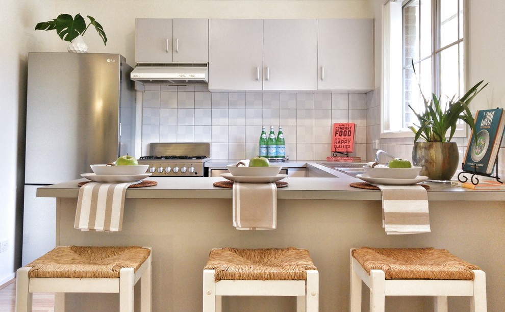 Design ideas for a small beach style u-shaped eat-in kitchen in Melbourne with a double-bowl sink, beaded inset cabinets, grey cabinets, laminate benchtops, grey splashback, ceramic splashback, stainless steel appliances, light hardwood floors and with island.