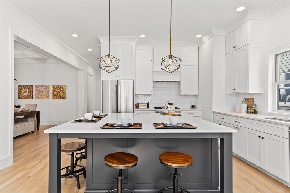 Example of a mid-sized minimalist l-shaped light wood floor open concept kitchen design in Columbus with an undermount sink, shaker cabinets, white cabinets, quartz countertops, white backsplash, ceramic backsplash, stainless steel appliances, an island and white countertops