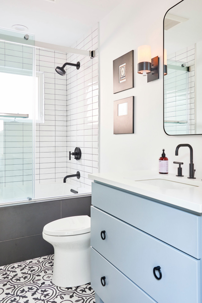 Photo of a mid-sized contemporary master bathroom in Chicago with white walls, ceramic floors, white floor, blue cabinets, a shower/bathtub combo, granite benchtops, a sliding shower screen, a single vanity, flat-panel cabinets, an alcove tub, white tile, subway tile, an undermount sink, white benchtops, a freestanding vanity and a two-piece toilet.