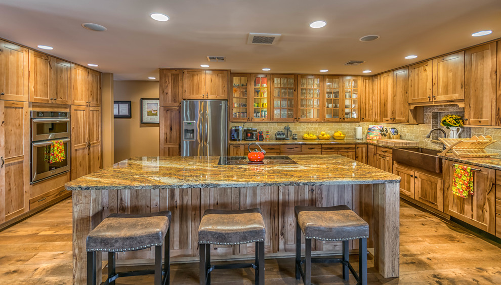 Open concept kitchen - large rustic u-shaped medium tone wood floor open concept kitchen idea in Phoenix with a farmhouse sink, shaker cabinets, medium tone wood cabinets, granite countertops, beige backsplash, stone tile backsplash, stainless steel appliances and an island
