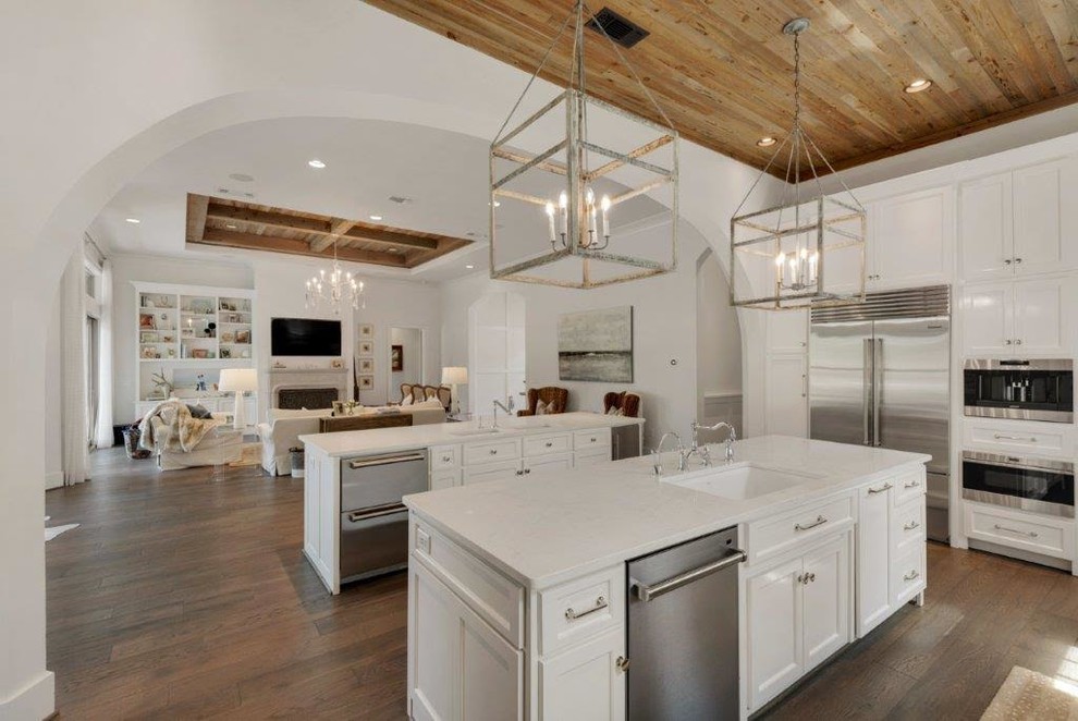 Photo of an expansive country u-shaped open plan kitchen in Miami with shaker cabinets, white cabinets, quartz benchtops, white splashback, multiple islands, an undermount sink, stone slab splashback, stainless steel appliances and medium hardwood floors.