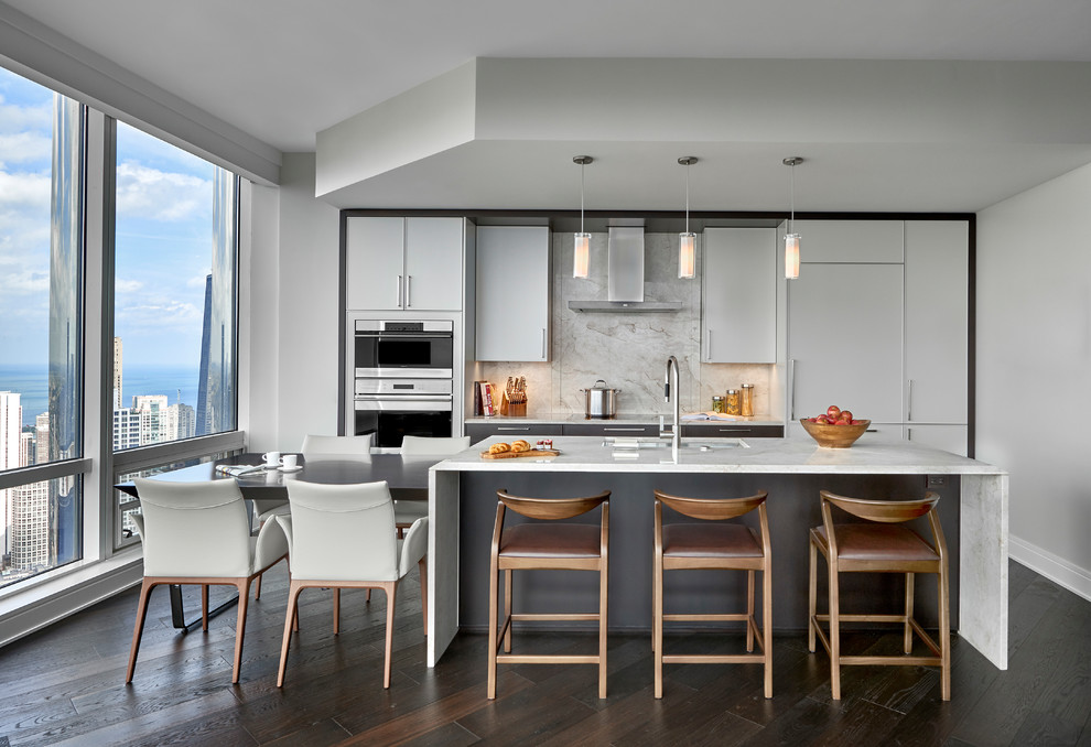 Inspiration for a contemporary eat-in kitchen in Chicago with an undermount sink, flat-panel cabinets, white cabinets, stone slab splashback, stainless steel appliances, dark hardwood floors, with island, brown floor and white benchtop.