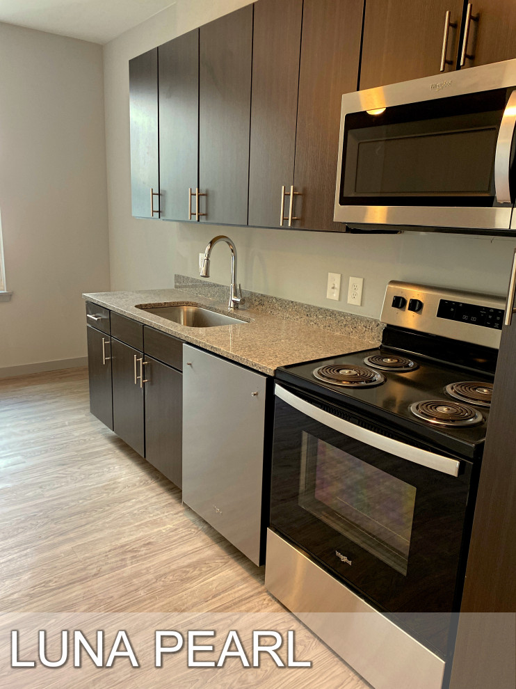 This is an example of a large modern l-shaped eat-in kitchen in Atlanta with a drop-in sink, flat-panel cabinets, dark wood cabinets, granite benchtops, grey splashback, granite splashback, stainless steel appliances, laminate floors, with island, grey floor and grey benchtop.