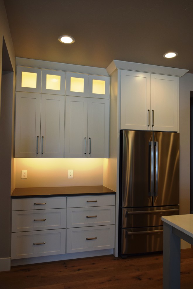 Open concept kitchen - transitional l-shaped medium tone wood floor open concept kitchen idea with a farmhouse sink, shaker cabinets, white cabinets, quartz countertops, gray backsplash, subway tile backsplash, stainless steel appliances and an island