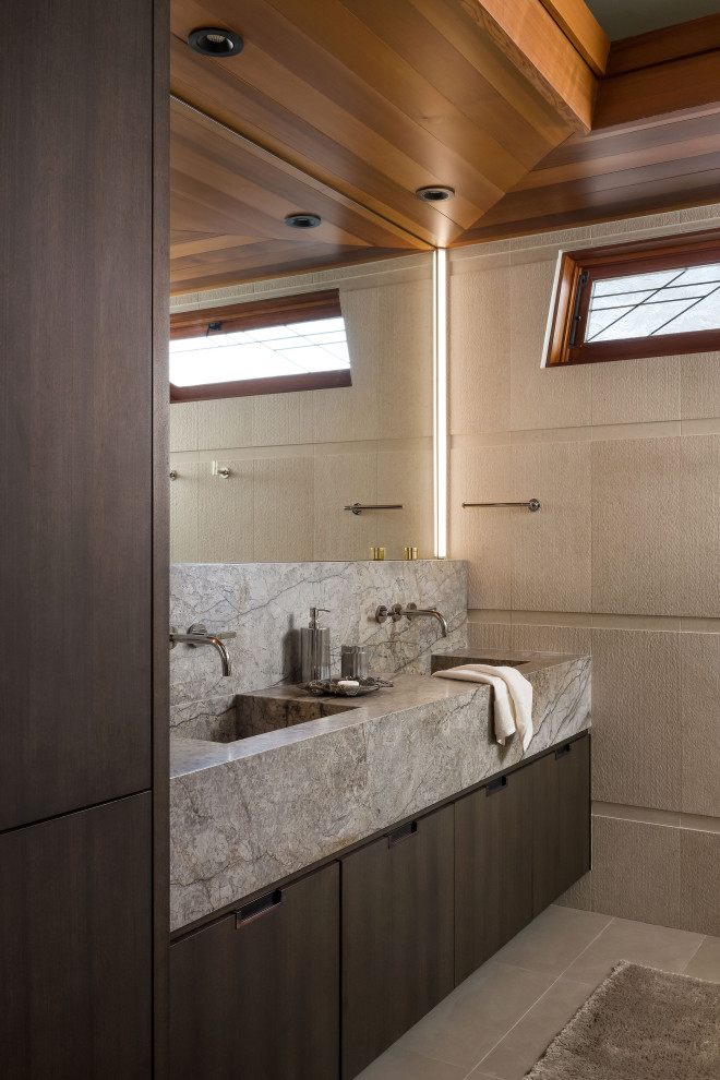 Пример оригинального дизайна: ванная комната среднего размера в стиле модернизм с плоскими фасадами, темными деревянными фасадами, душем без бортиков, бежевой плиткой, плиткой из известняка, полом из известняка, монолитной раковиной, мраморной столешницей, душем с распашными дверями, серой столешницей, тумбой под две раковины и деревянным потолком