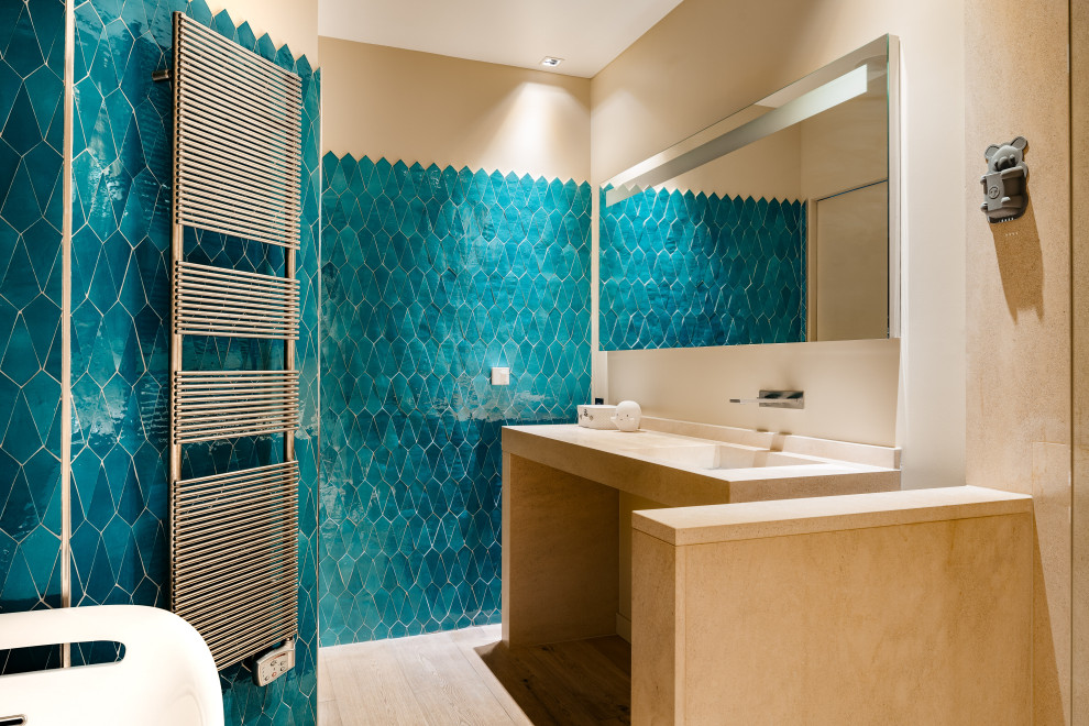 Foto de cuarto de baño actual con combinación de ducha y bañera, baldosas y/o azulejos azules, baldosas y/o azulejos en mosaico, paredes azules, suelo de madera clara, lavabo integrado y suelo beige