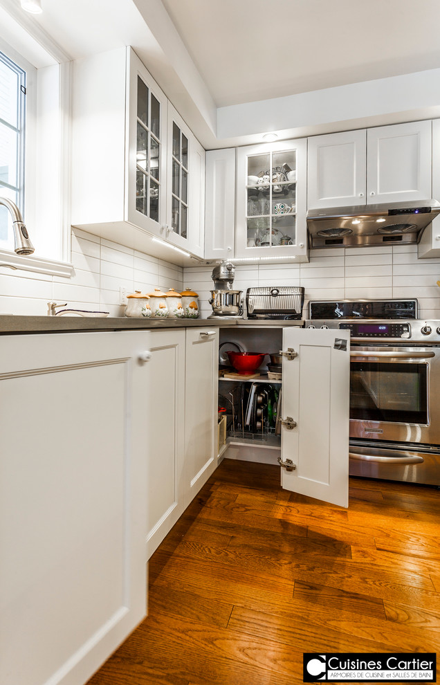 Example of a large transitional medium tone wood floor eat-in kitchen design in Montreal with a double-bowl sink, shaker cabinets, white cabinets, quartzite countertops, white backsplash, ceramic backsplash, stainless steel appliances and an island
