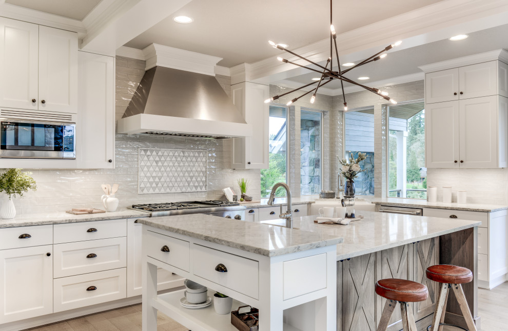 Photo of a large transitional u-shaped eat-in kitchen in Portland with a farmhouse sink, shaker cabinets, white cabinets, quartz benchtops, grey splashback, ceramic splashback, stainless steel appliances, light hardwood floors, with island, grey floor and white benchtop.