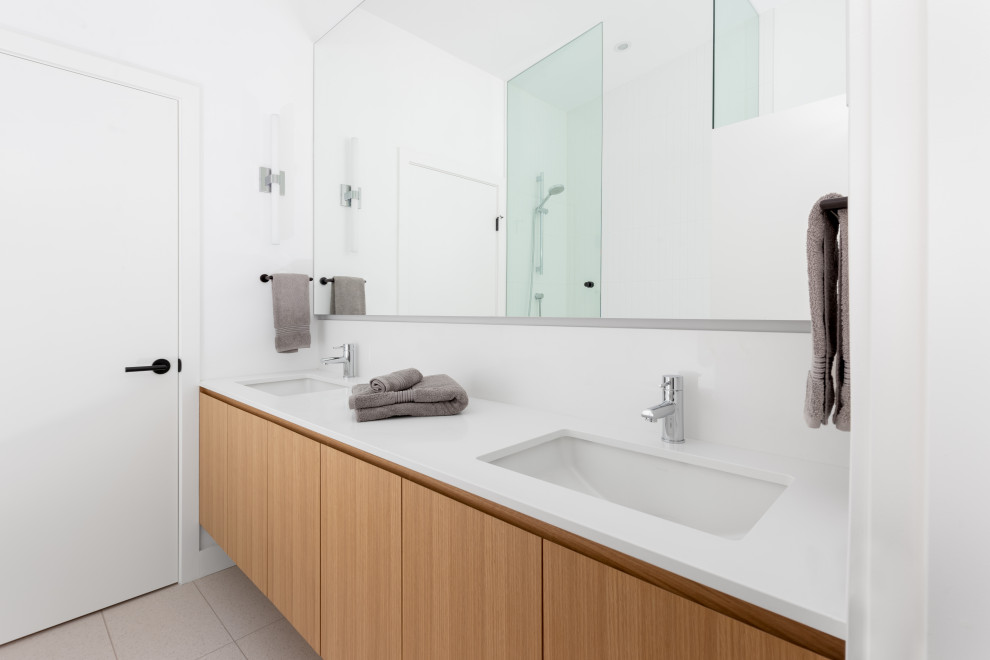 Modelo de cuarto de baño principal, doble, flotante y blanco actual de tamaño medio con puertas de armario de madera clara, paredes blancas, lavabo encastrado, suelo beige, encimeras blancas y armarios con paneles lisos