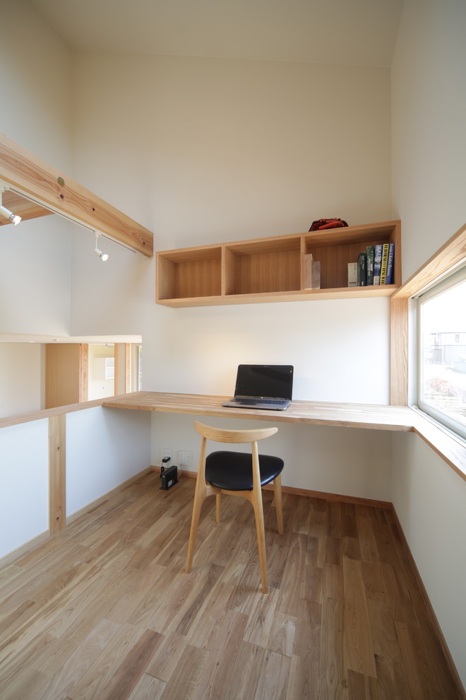 This is an example of a small scandinavian study room in Other with white walls, medium hardwood floors, a built-in desk and brown floor.