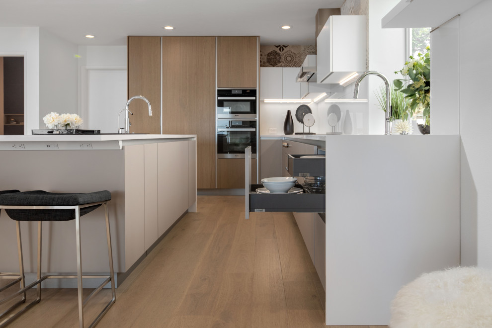 Inspiration for a large contemporary l-shaped open plan kitchen in Tampa with an undermount sink, flat-panel cabinets, grey cabinets, quartz benchtops, green splashback, glass sheet splashback, black appliances, medium hardwood floors, with island, brown floor and white benchtop.