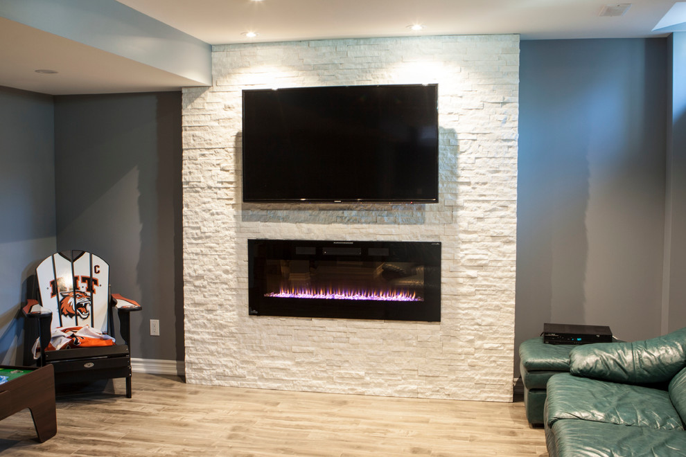 Design ideas for a mid-sized modern look-out basement in Toronto with grey walls, a standard fireplace, a stone fireplace surround, laminate floors and beige floor.