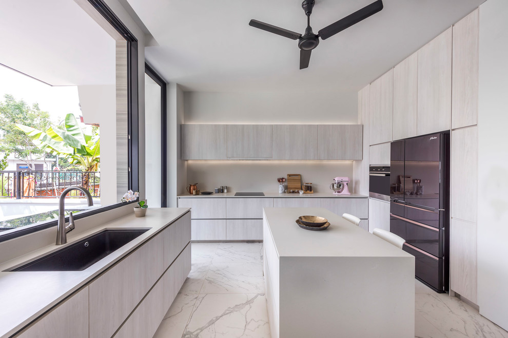 This is an example of a contemporary u-shaped separate kitchen in Singapore with an undermount sink, flat-panel cabinets, beige cabinets, white splashback, black appliances, with island, white floor and white benchtop.