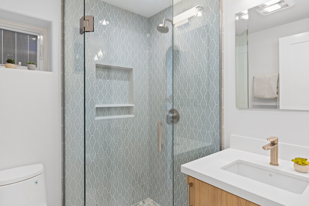 Inspiration for a small transitional kids bathroom in San Diego with flat-panel cabinets, light wood cabinets, a corner shower, a one-piece toilet, blue tile, ceramic tile, grey walls, porcelain floors, an undermount sink, engineered quartz benchtops, grey floor, a hinged shower door and white benchtops.