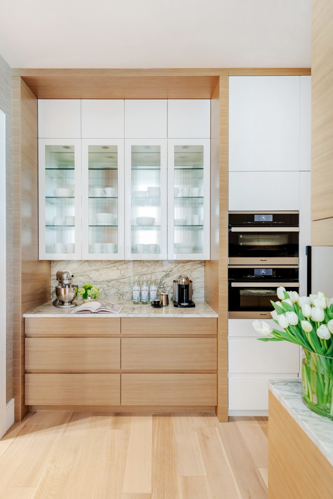 Large trendy l-shaped light wood floor and beige floor kitchen pantry photo with an undermount sink, flat-panel cabinets, light wood cabinets, marble countertops, white backsplash, stone slab backsplash, paneled appliances, an island and white countertops