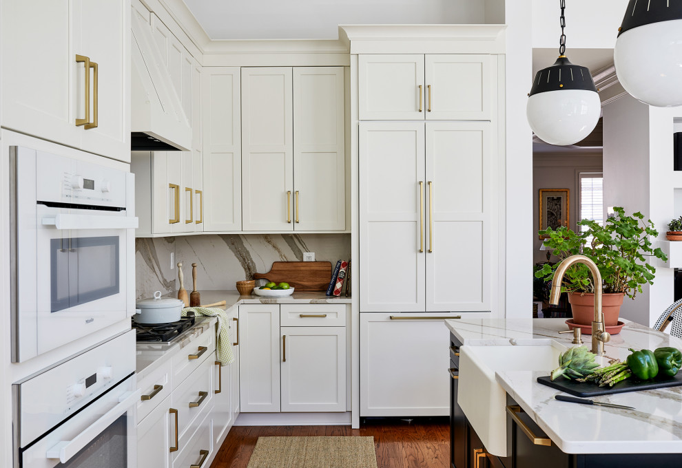 Mid-sized transitional l-shaped open plan kitchen in Chicago with a farmhouse sink, recessed-panel cabinets, white cabinets, quartz benchtops, white splashback, engineered quartz splashback, white appliances, medium hardwood floors, with island, brown floor and white benchtop.