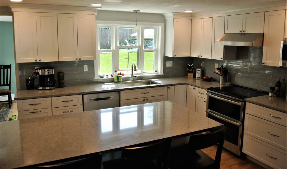 Example of a transitional light wood floor kitchen design in Boston with an undermount sink, shaker cabinets, white cabinets, quartz countertops, gray backsplash, subway tile backsplash, stainless steel appliances, an island and gray countertops