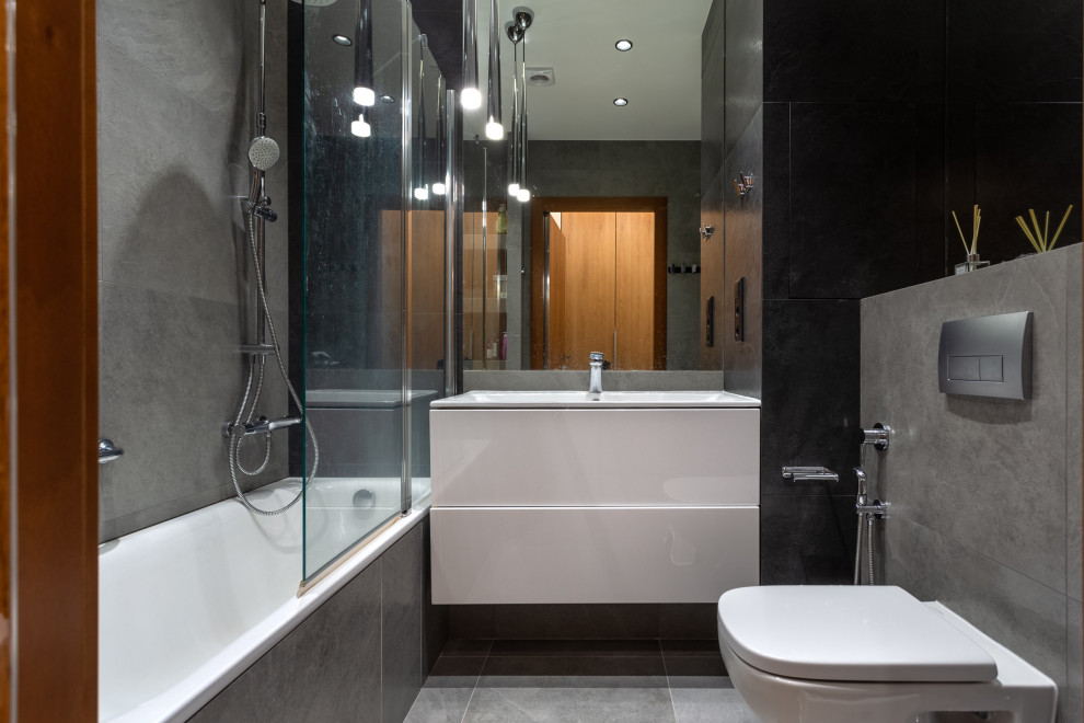 Стильный дизайн: маленькая серо-белая ванная комната в стиле фьюжн с плоскими фасадами, белыми фасадами, ванной в нише, душем над ванной, инсталляцией, черной плиткой, керамогранитной плиткой, серыми стенами, полом из керамогранита, душевой кабиной, подвесной раковиной, столешницей из кварцита, серым полом, душем с раздвижными дверями, белой столешницей, гигиеническим душем, тумбой под одну раковину и подвесной тумбой для на участке и в саду - последний тренд