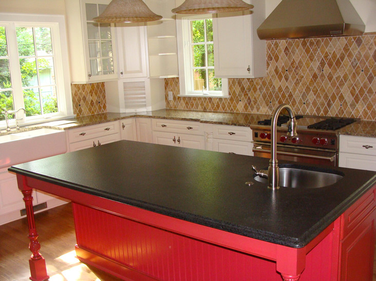 L-shaped medium tone wood floor enclosed kitchen photo with a farmhouse sink, white cabinets, granite countertops, beige backsplash, stainless steel appliances and an island