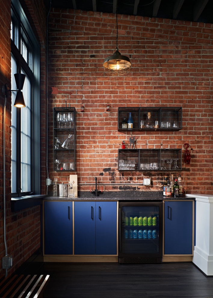 Cette image montre un bar de salon avec évier urbain avec un évier encastré, un placard à porte plane, des portes de placard bleues, un plan de travail en granite, une crédence en brique, un sol en vinyl, un sol gris et un plan de travail gris.