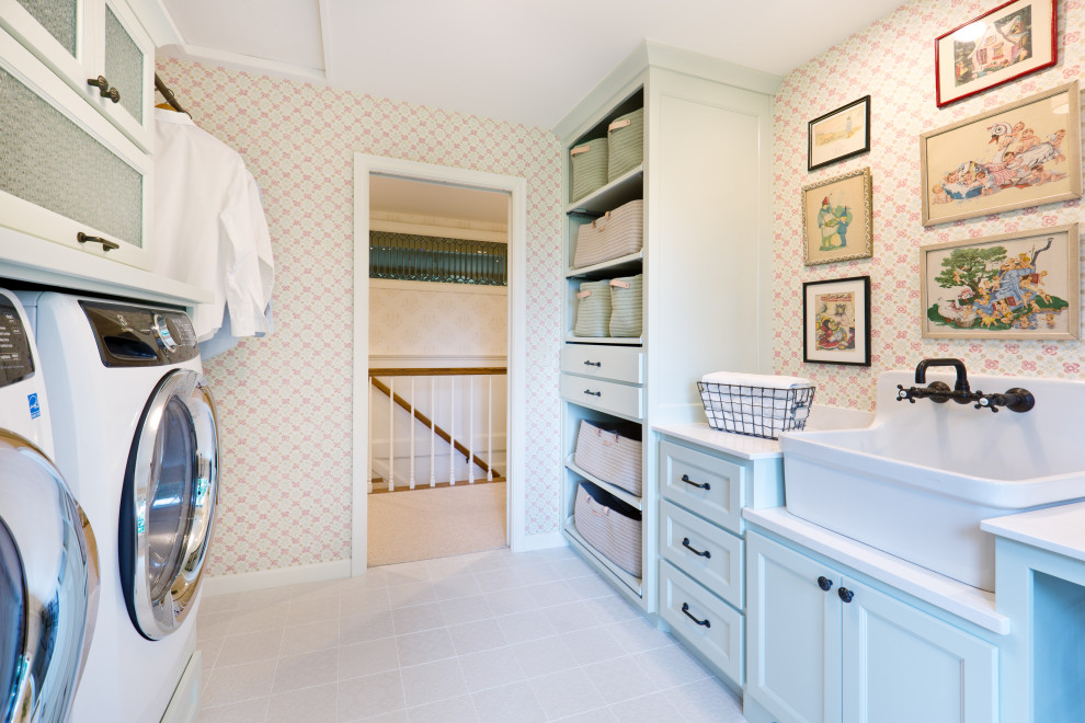 This is an example of a mid-sized traditional single-wall dedicated laundry room in Minneapolis with a farmhouse sink, flat-panel cabinets, green cabinets, quartz benchtops, mosaic tile splashback, multi-coloured walls, porcelain floors, a side-by-side washer and dryer, white floor, white benchtop and wallpaper.