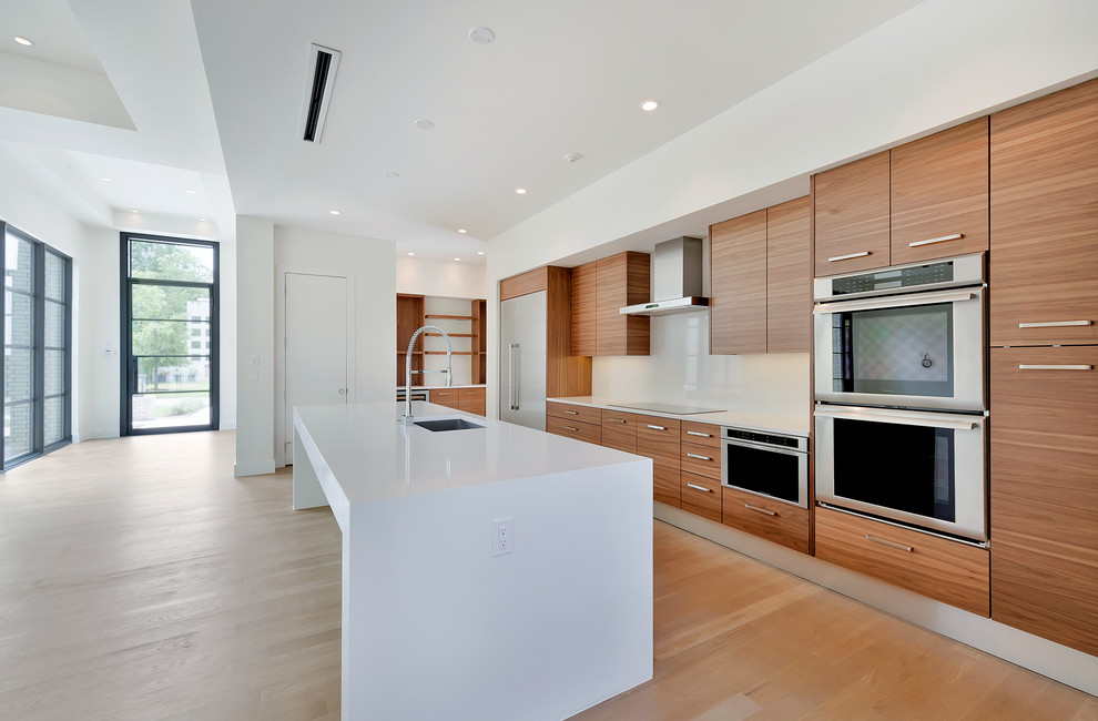 Inspiration for a large contemporary single-wall kitchen in Dallas with an undermount sink, flat-panel cabinets, medium wood cabinets, solid surface benchtops, stainless steel appliances, light hardwood floors and with island.