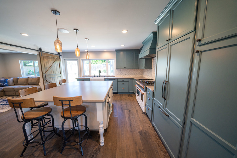Photo of a large country l-shaped eat-in kitchen in Orange County with a farmhouse sink, recessed-panel cabinets, blue cabinets, white splashback, marble splashback, panelled appliances, dark hardwood floors, with island, brown floor and beige benchtop.