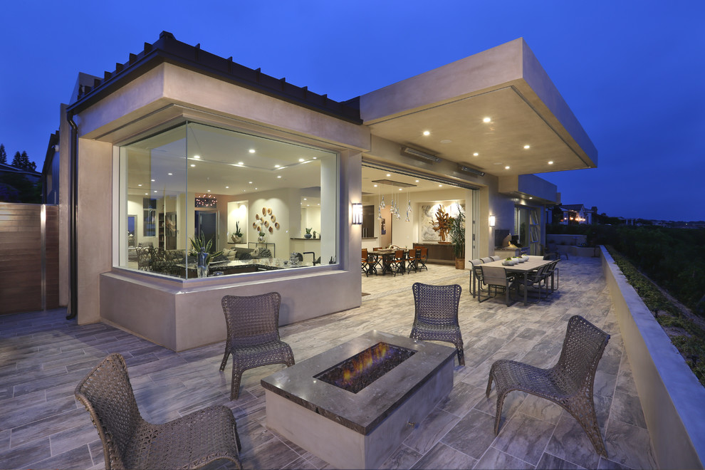 Mid-sized transitional backyard patio in Orange County with a fire feature, tile and a roof extension.