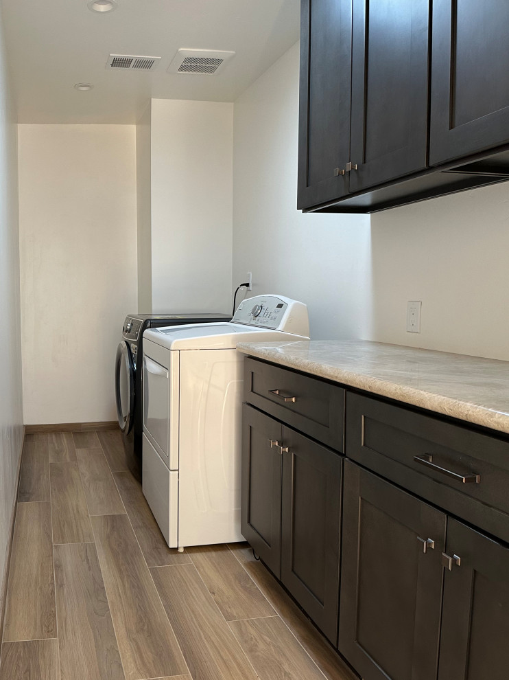 Inspiration for a mid-sized transitional single-wall laundry room in San Francisco with shaker cabinets, black cabinets, quartzite benchtops, white walls, ceramic floors, a side-by-side washer and dryer, brown floor and beige benchtop.