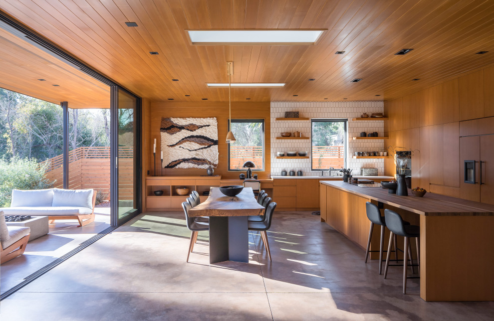 Inspiration for a mid-sized midcentury l-shaped open plan kitchen in San Francisco with an undermount sink, flat-panel cabinets, medium wood cabinets, wood benchtops, white splashback, subway tile splashback, black appliances, concrete floors, with island, grey floor, brown benchtop and wood.