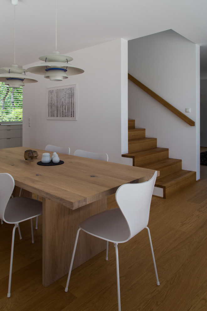 Réalisation d'une salle à manger ouverte sur le salon design avec un mur blanc et un sol en bois brun.