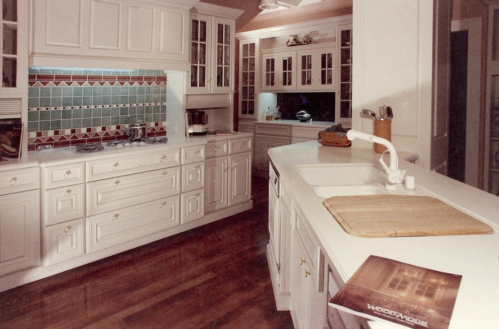 Design ideas for a mid-sized traditional separate kitchen in San Luis Obispo with an integrated sink, raised-panel cabinets, white cabinets, solid surface benchtops, multi-coloured splashback, ceramic splashback, dark hardwood floors and a peninsula.