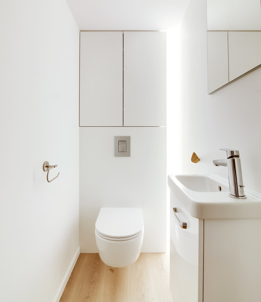 Photo of a small modern powder room in Strasbourg with beaded inset cabinets, white cabinets, a wall-mount toilet, white walls, laminate floors and a wall-mount sink.