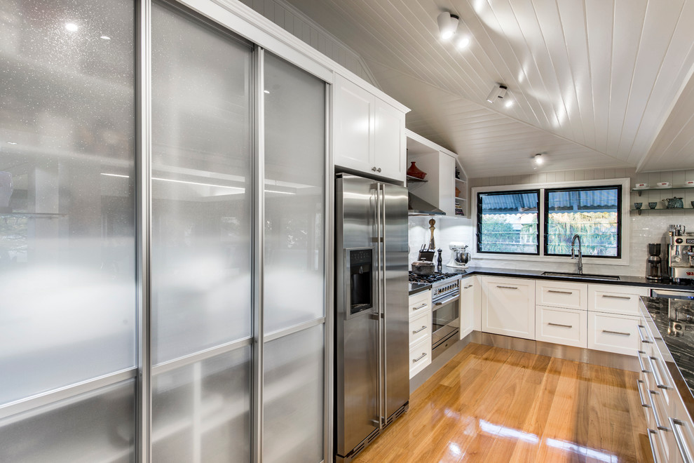 This is an example of a contemporary l-shaped open plan kitchen in Brisbane with shaker cabinets, white cabinets, white splashback, subway tile splashback and stainless steel appliances.