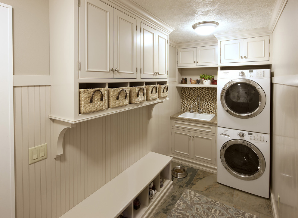 Design ideas for a mid-sized transitional single-wall utility room in Miami with a drop-in sink, recessed-panel cabinets, white cabinets, granite benchtops, beige walls, slate floors, a stacked washer and dryer, grey floor and beige benchtop.