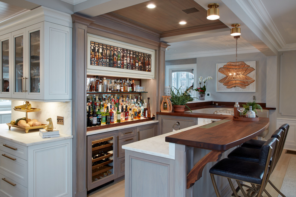 Inspiration for a large traditional home bar in New York with recessed-panel cabinets, white cabinets, marble worktops, light hardwood flooring, white worktops and beige floors.