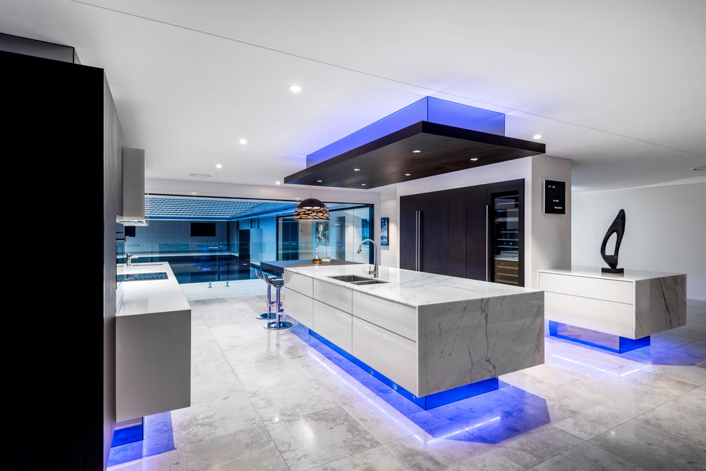 This is an example of an expansive contemporary galley open plan kitchen in Brisbane with an undermount sink, glass-front cabinets, beige cabinets, marble benchtops, black splashback, mirror splashback, black appliances, travertine floors, with island and beige floor.