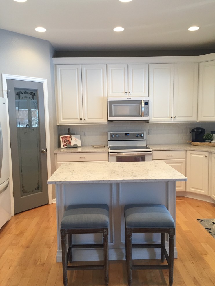 Large transitional u-shaped light wood floor and beige floor open concept kitchen photo in Denver with a farmhouse sink, raised-panel cabinets, white cabinets, quartz countertops, white backsplash, ceramic backsplash, white appliances and an island