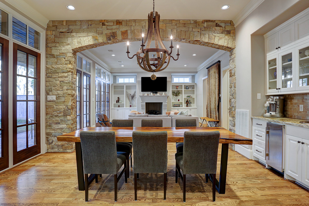 Traditional open plan dining in Houston with beige walls, light hardwood floors, a standard fireplace, a concrete fireplace surround and brown floor.