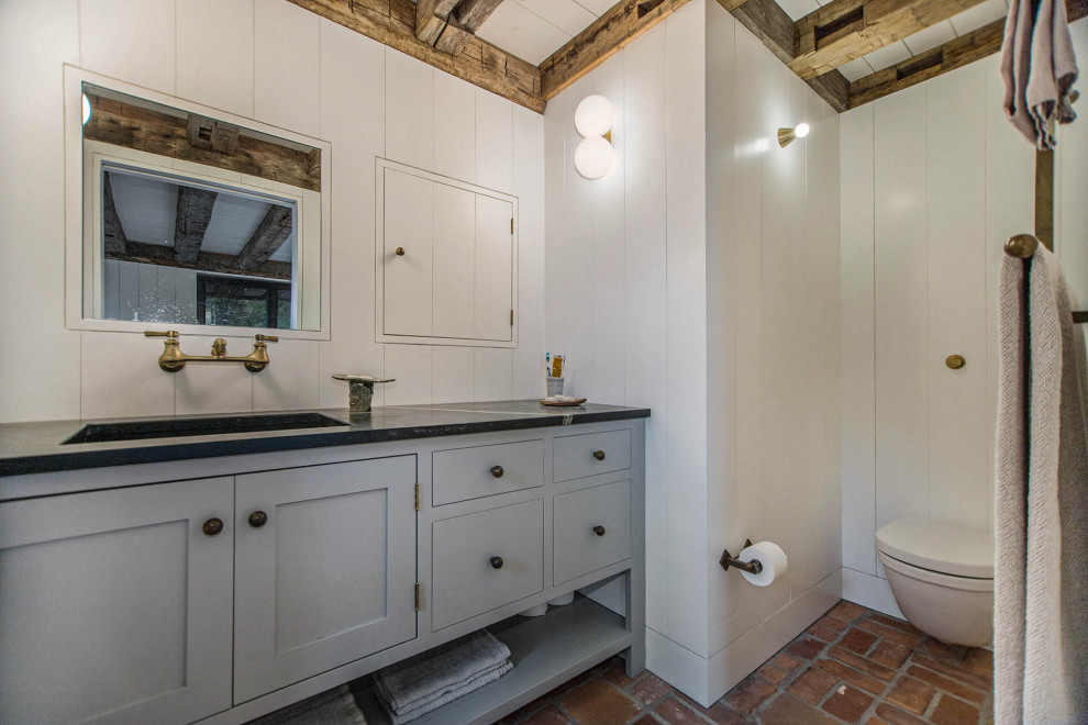 Exemple d'une salle de bain montagne avec un placard à porte plane, des portes de placard grises, WC suspendus, un mur blanc, un sol en brique, un lavabo encastré, un sol rouge, un plan de toilette noir, meuble simple vasque et du lambris de bois.