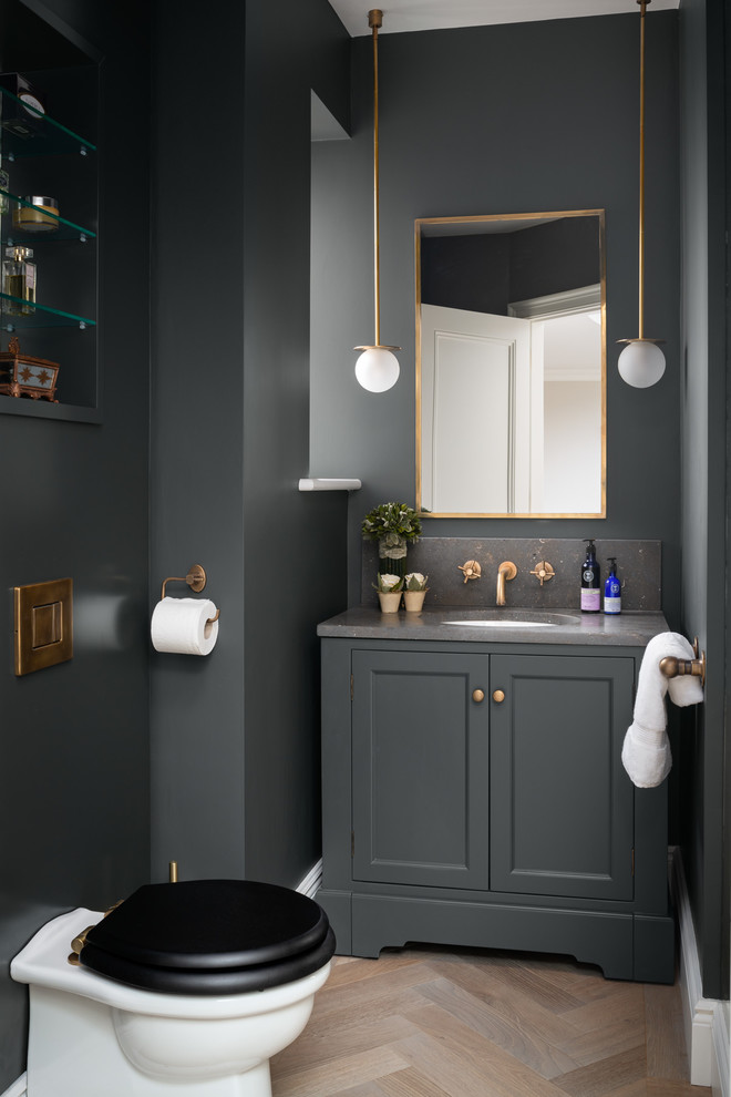 Photo of a mid-sized transitional powder room in London with a one-piece toilet, light hardwood floors, limestone benchtops, grey benchtops, recessed-panel cabinets, grey cabinets, grey walls, an undermount sink and beige floor.